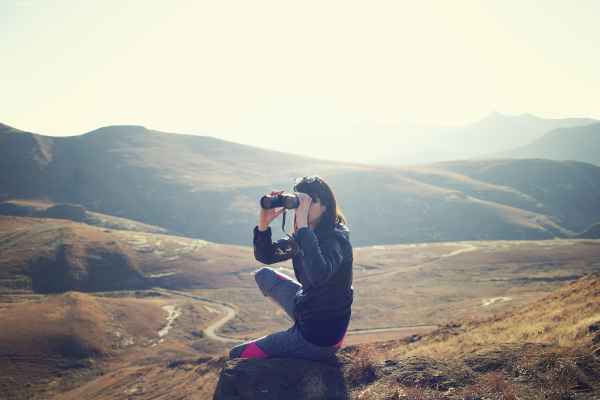 An adventurer in hilly plains looking through binoculars.