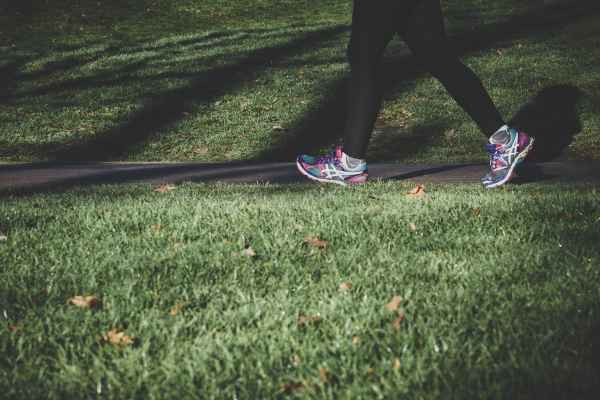 A person in athletic shoes walking through a park.